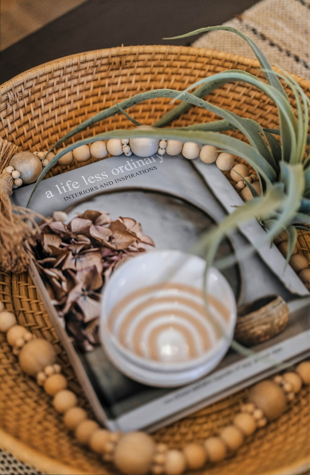 Woven tray with a ceramic cup, design book, beads, and greenery