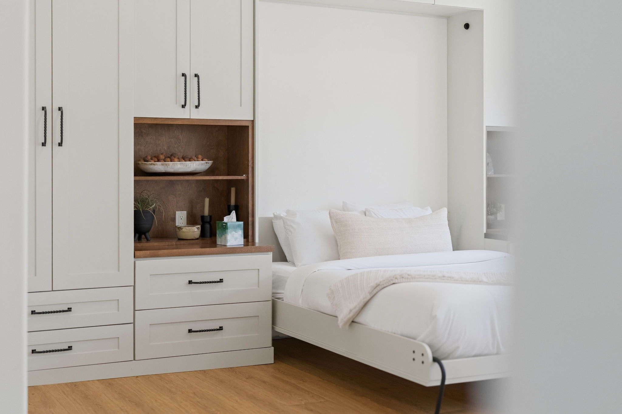 Inviting bedroom with white bedding, built-in white cabinets, and warm wood shelving