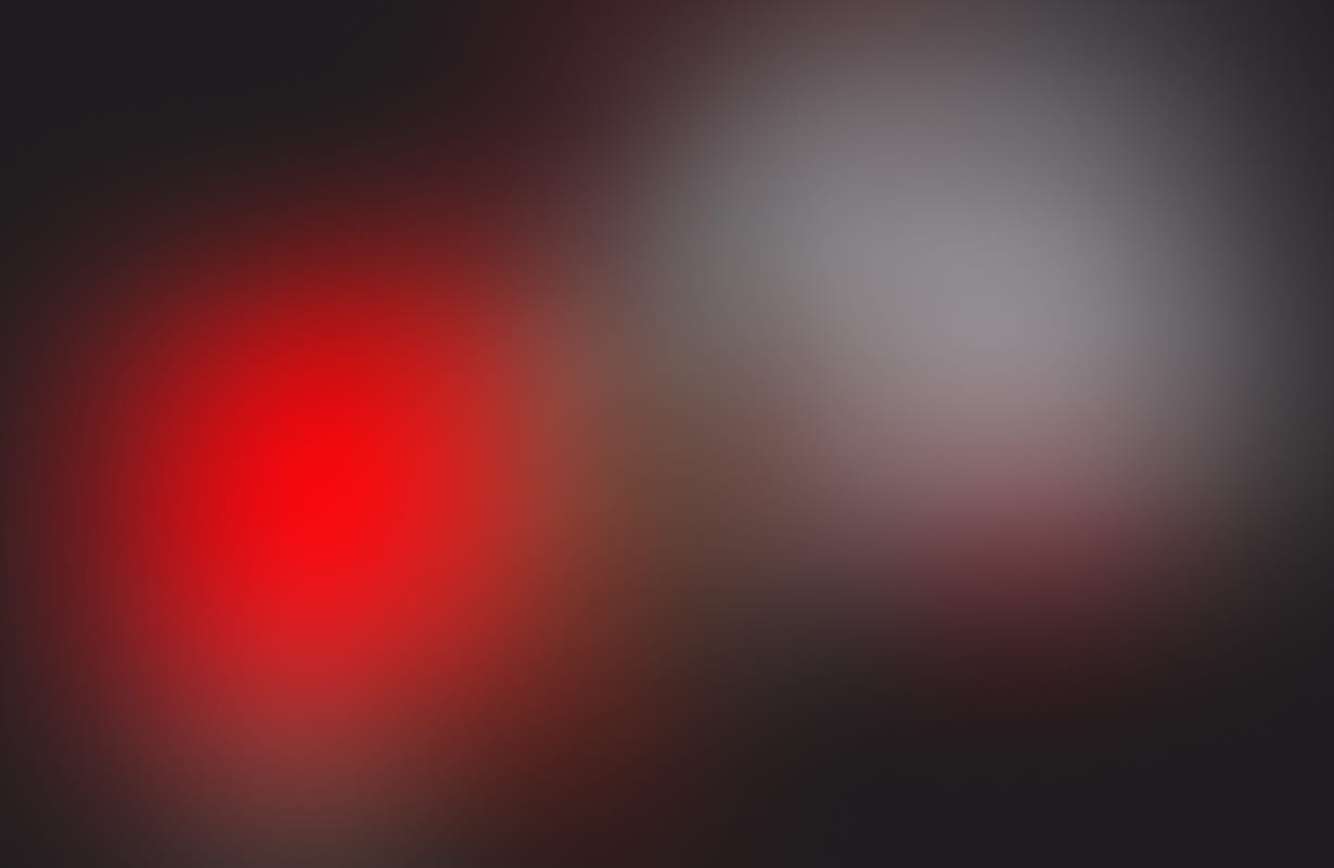 Blurry image with indistinct red and gray shapes on a dark background.