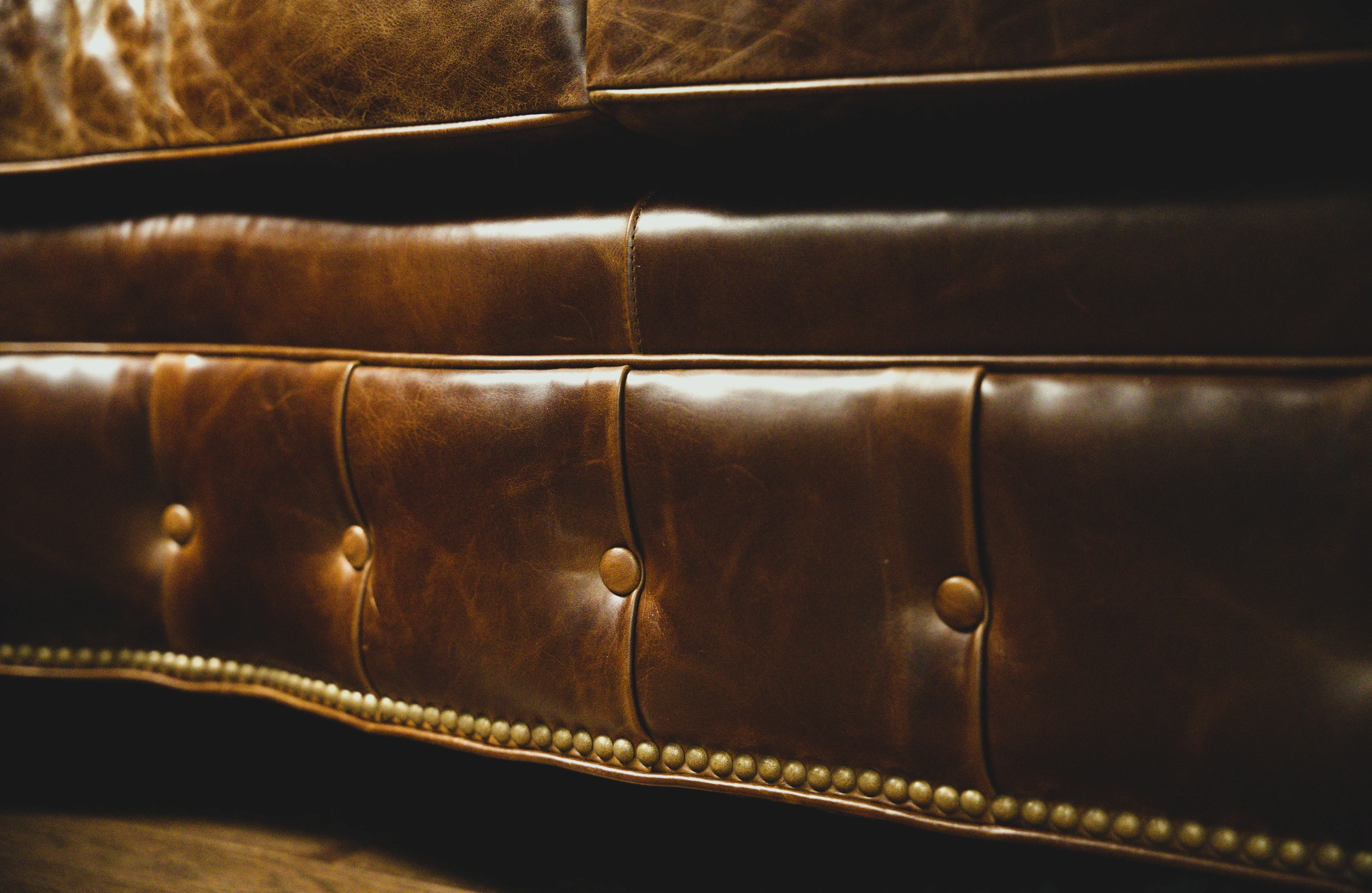 Close detail of the London Pub piece: warm brown leather, button tufting, stitched seams, and brass nailhead trim