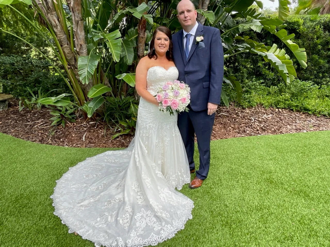 Photo of a happy couple at their wedding on a well manicured green lawn.