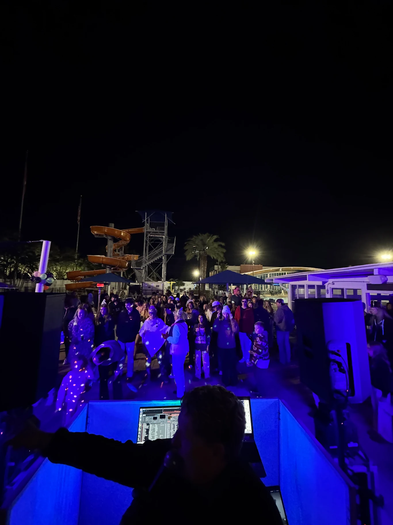 Photo of our DJ behind his booth looking out into the crowd dancing during an outdoor, nighttime glow party.