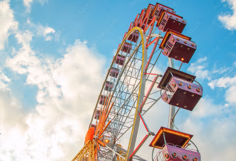 Large Ferris wheel with purple cabins against a partly cloudy blue sky.