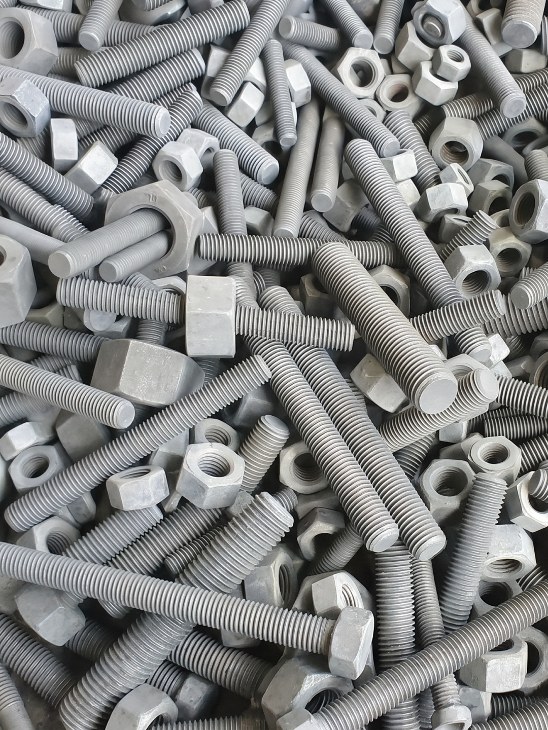 Pile of hex nuts and threaded bolts in various sizes with a gray phosphate finish.