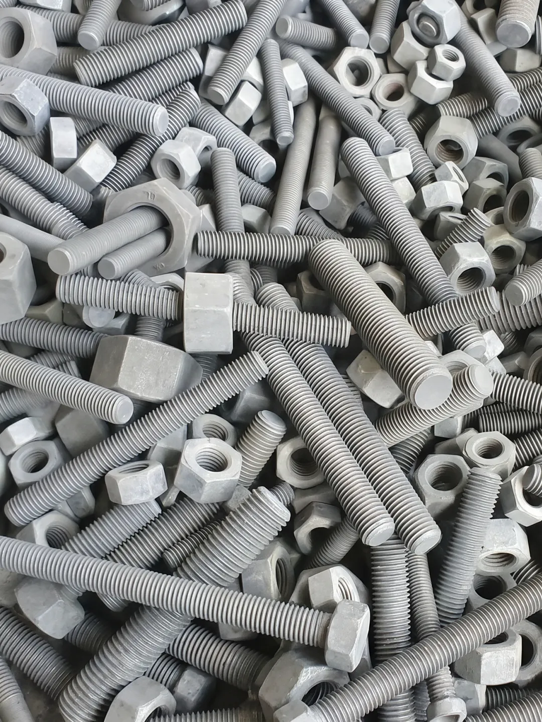 Pile of hex nuts and threaded bolts in various sizes with a gray phosphate finish.