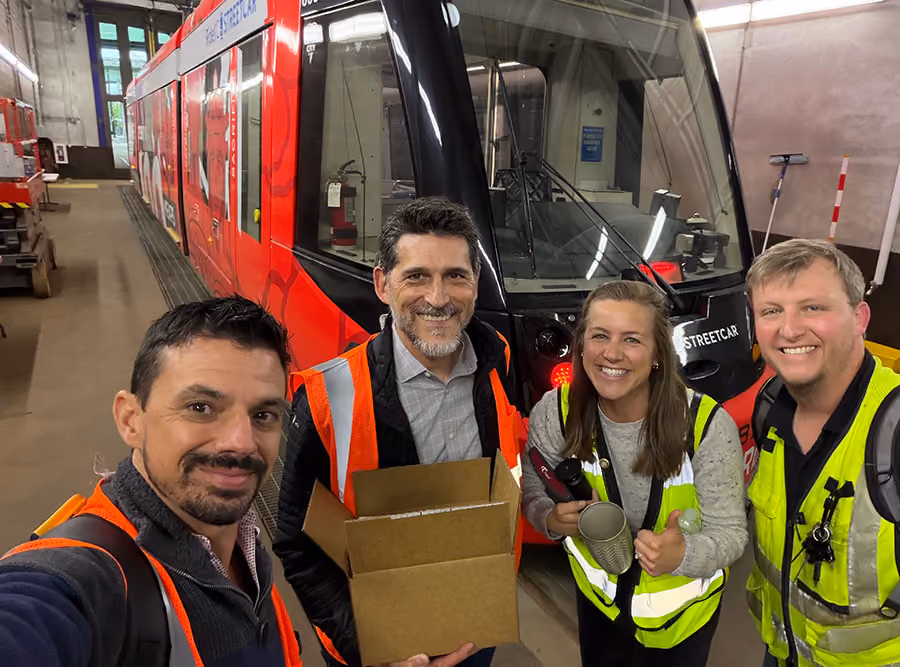 Group photo of Swiftly employees with a red rail vehicle during a RideKC site visit.