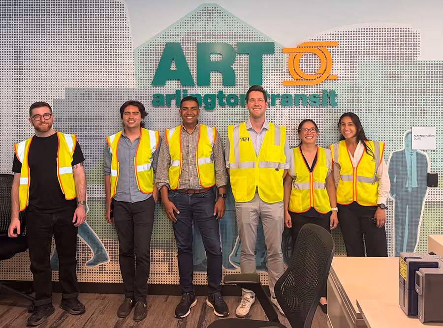 Group photo of Swiftly employees in yellow safety vests in front of an Arlington Transit (ART) sign during a site visit.
