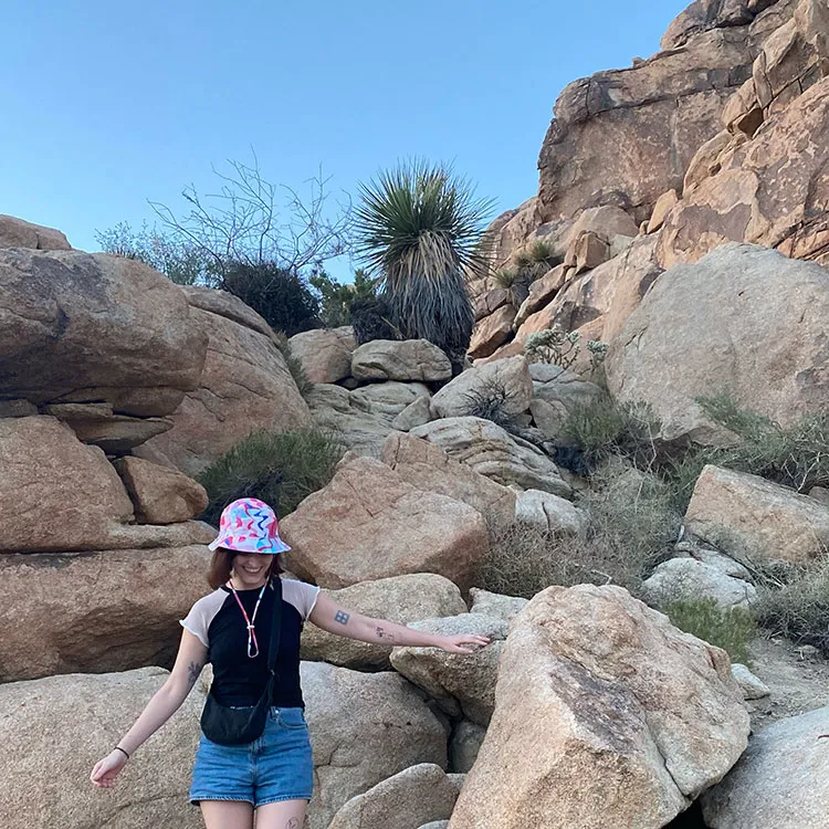 Swiftly employee Ella Morner-Ritt smiling while hiking among large boulders in a desert landscape.