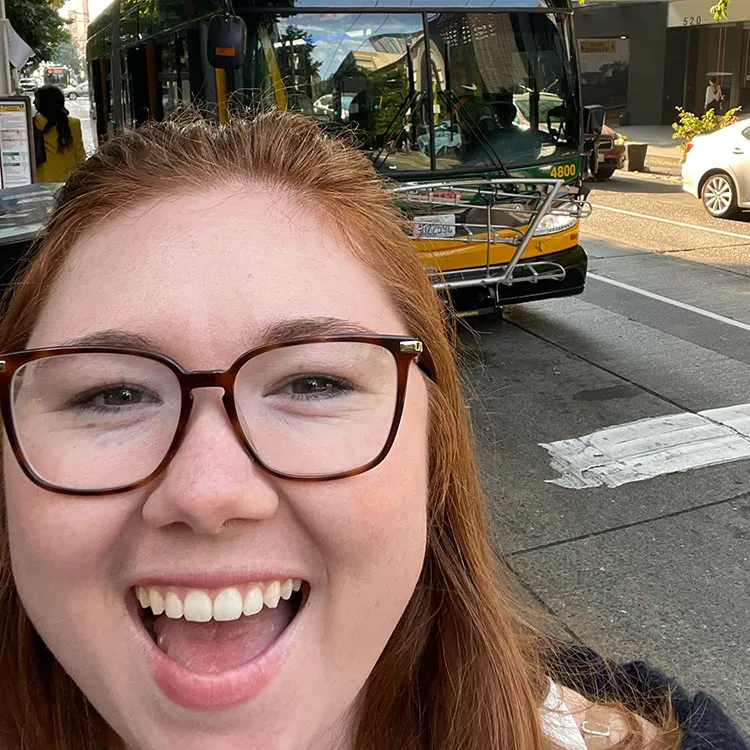 Swiftly employee Siena Guerrazzi smiling for a selfie with a city bus in the background.