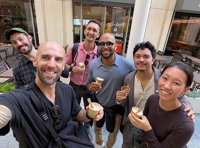 A group of six Swiftly employees smiling together outdoors, holding ice cream cones during a team offsite.