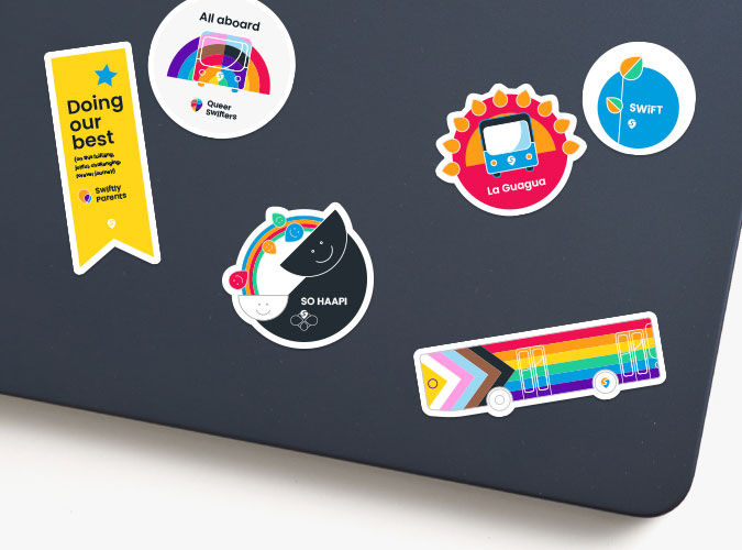 A laptop lid decorated with colorful stickers, including employee resource group logos and a bus decorated in progress pride flag colors.