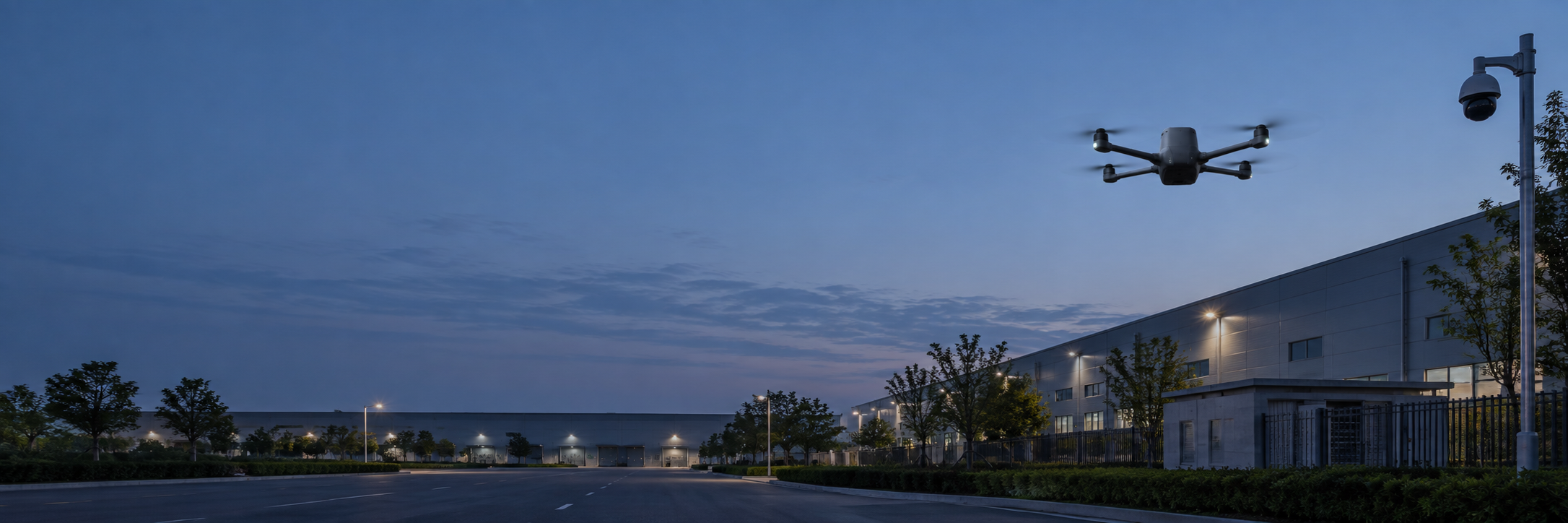 Rear view of a security drone over an industrial campus at dusk, with pole-mounted CCTV.