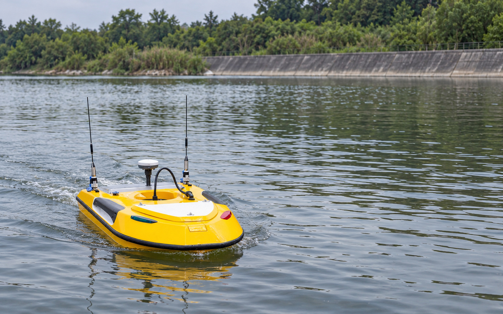 A compact yellow survey USV moving across a reservoir beside a concrete embankment.