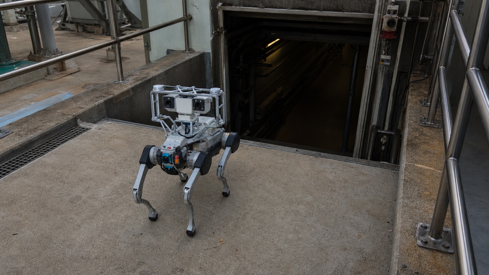 Quadruped inspection robot approaching a guarded industrial confined-space access route.