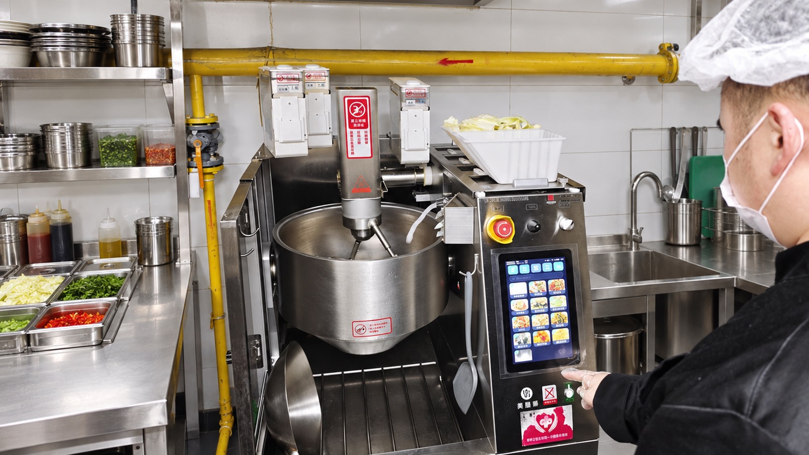 Operator at a cooking robot control panel in a commercial-kitchen setting.