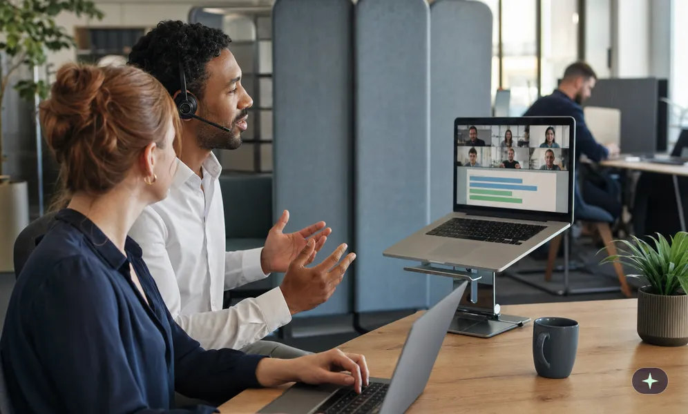 Mitarbeiter moderiert am Arbeitsplatz eine Videokonferenz, eine Kollegin startet als Co-Moderatorin eine Umfrage