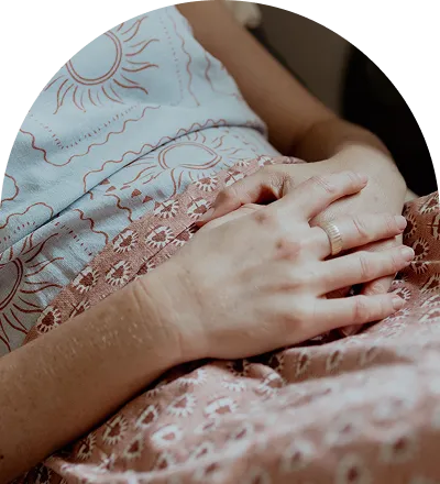 Close-up of a person's folded hands with a ring, resting on patterned fabric with sun designs.