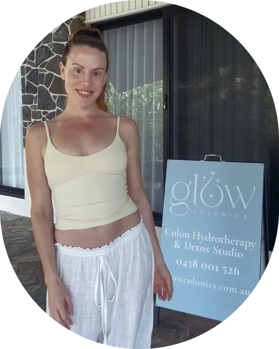 Steph from Glow Colonics standing beside colon hydrotherapy and detox studio signage in Cairns