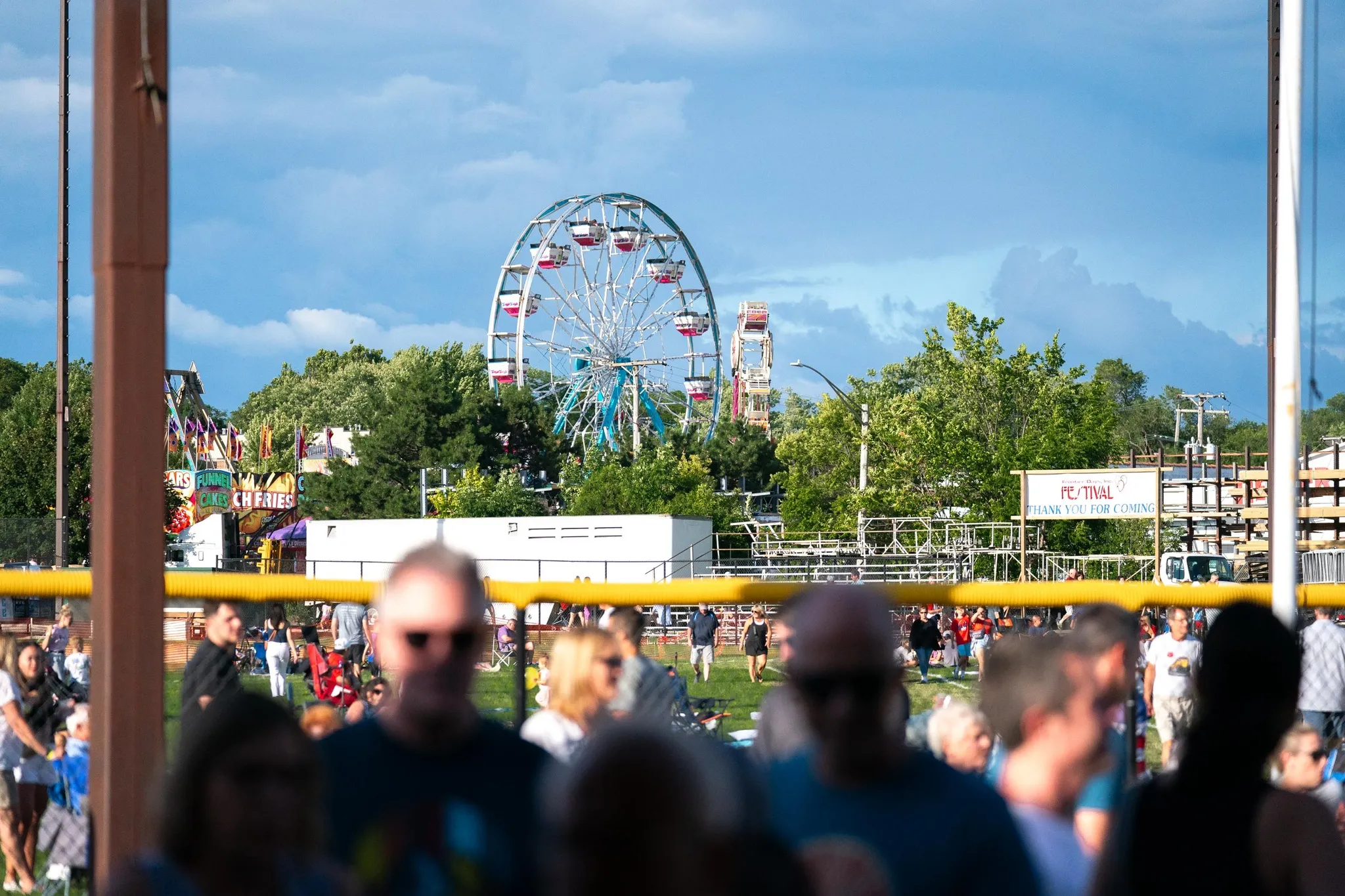 Crowd at the outdoor Frontier Days Festival with a Ferris wheel and food stands in the background under a blue sky.