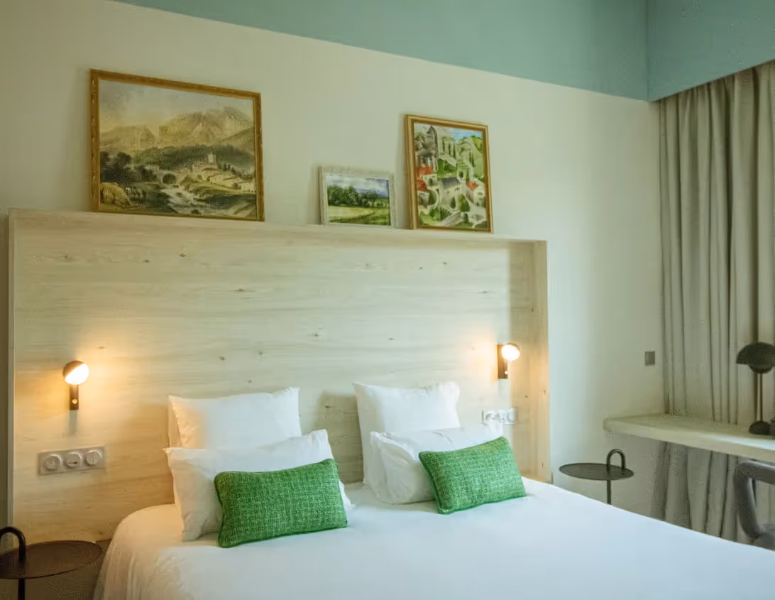 Tête de lit en bois clair avec tableaux alpins et coussins verts de la chambre supérieure hôtel Ysotop Grenoble.