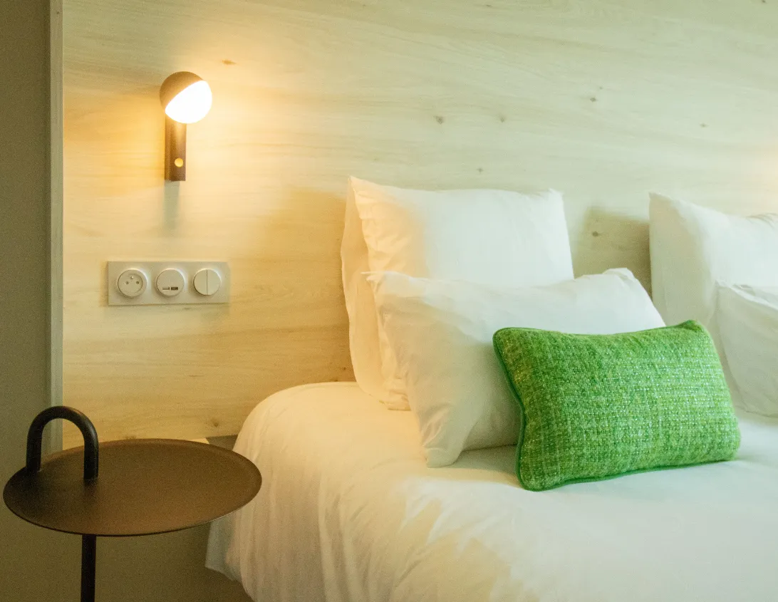 Lit douillet avec coussin vert et applique chaleureuse de la chambre supérieure hôtel Ysotop à Grenoble.