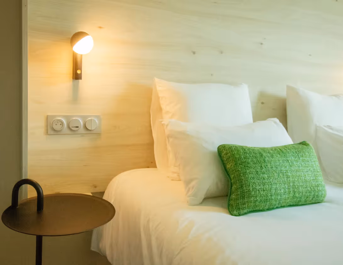 Lit moelleux avec coussin vert et applique chaleureuse dans le studio de l'hôtel Ysotop à Grenoble.