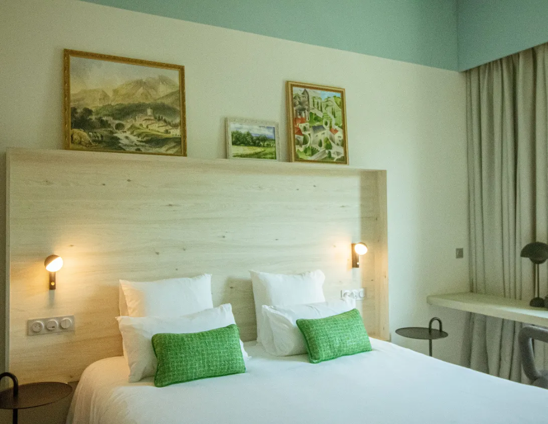 Light wood headboard with lighting and three alpine paintings in the large 4-star Ysotop Grenoble studio hotel.