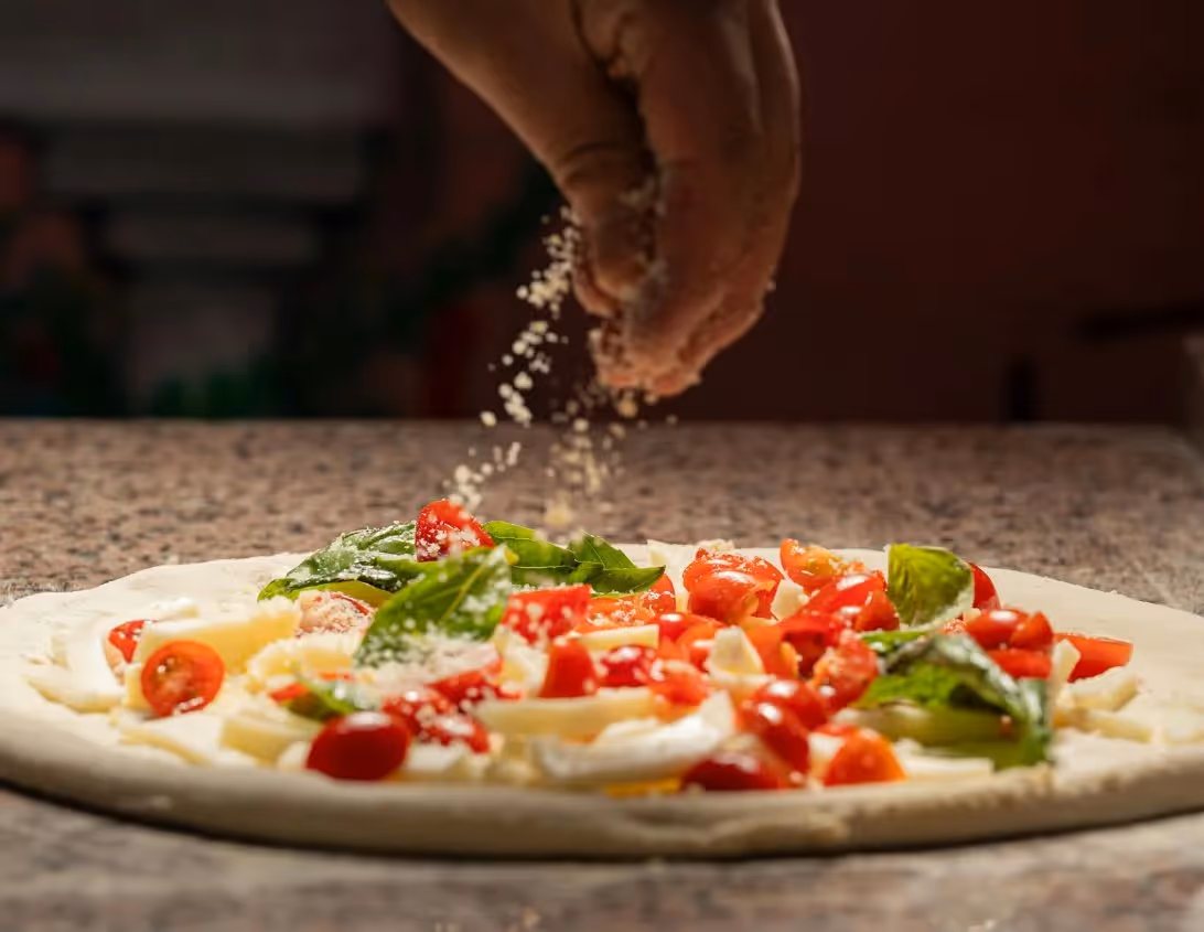 Chef saupoudrant du parmesan sur une pizza fraîche tomates cerises et basilic au restaurant Ysotop Grenoble.