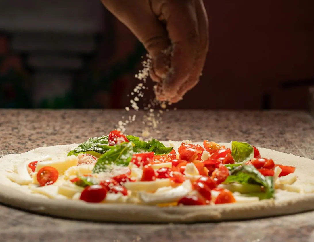 Chef sprinkling parmesan on a fresh cherry tomato and basil pizza at the Ysotop Grenoble restaurant.