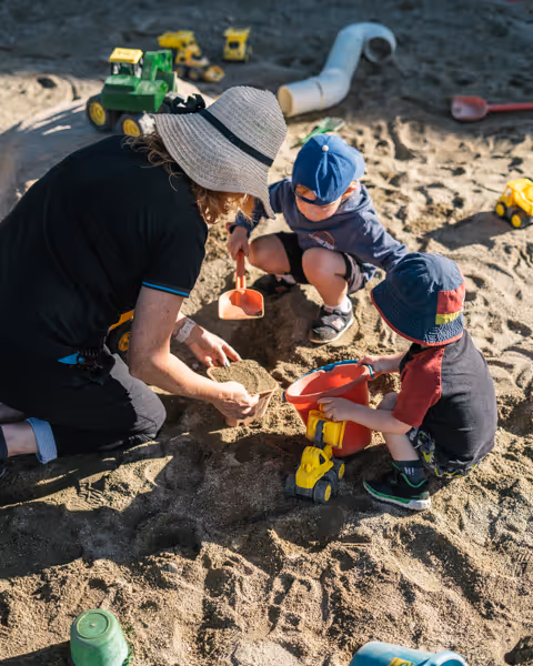 A kaiako digging in the sandpit with tamariki