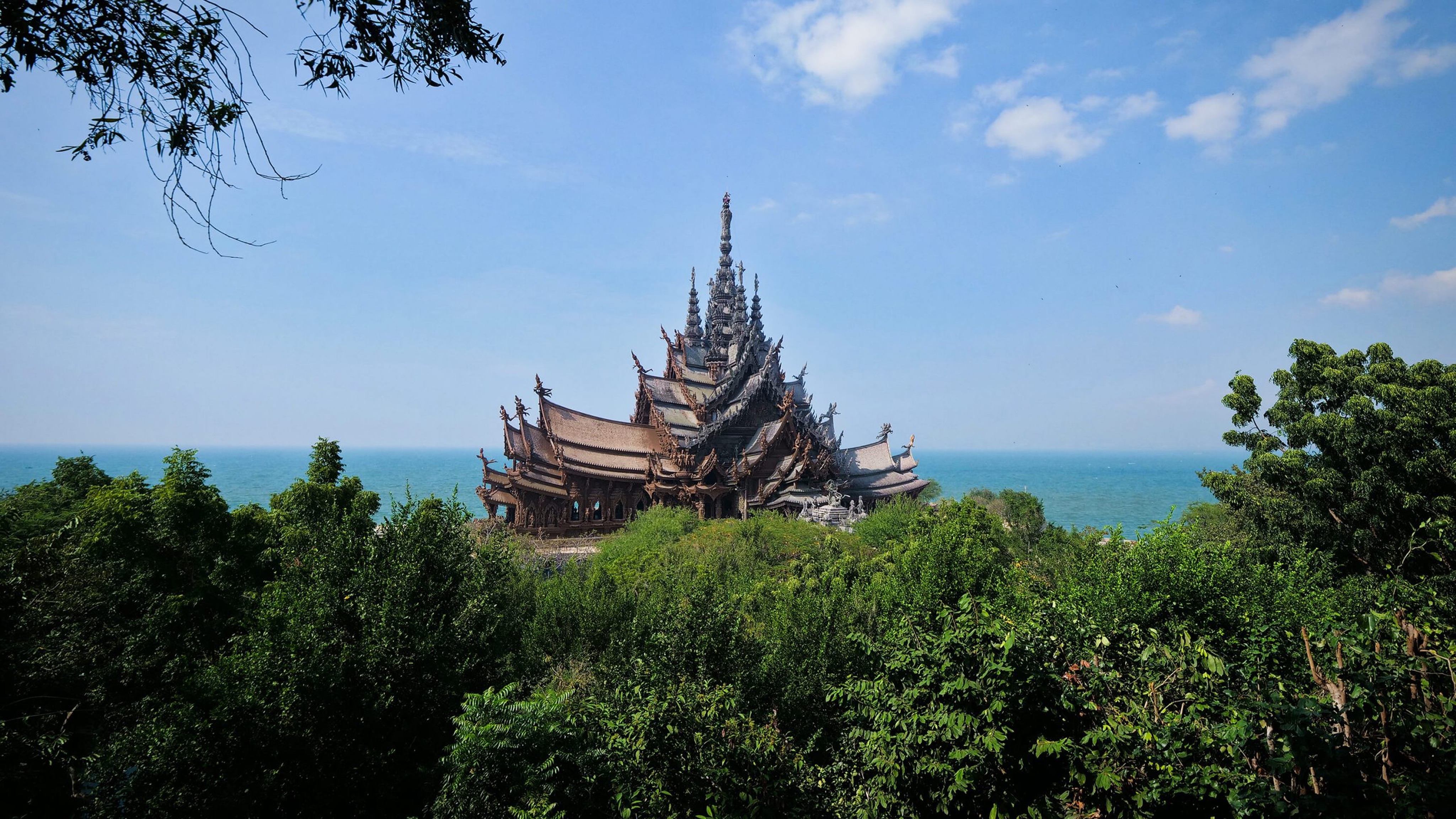 Large white Buddha statue surrounded by trees with ocean and coastline in the background.