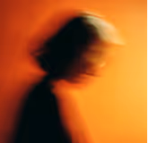 Blurred silhouette of a person with reddish-orange background.