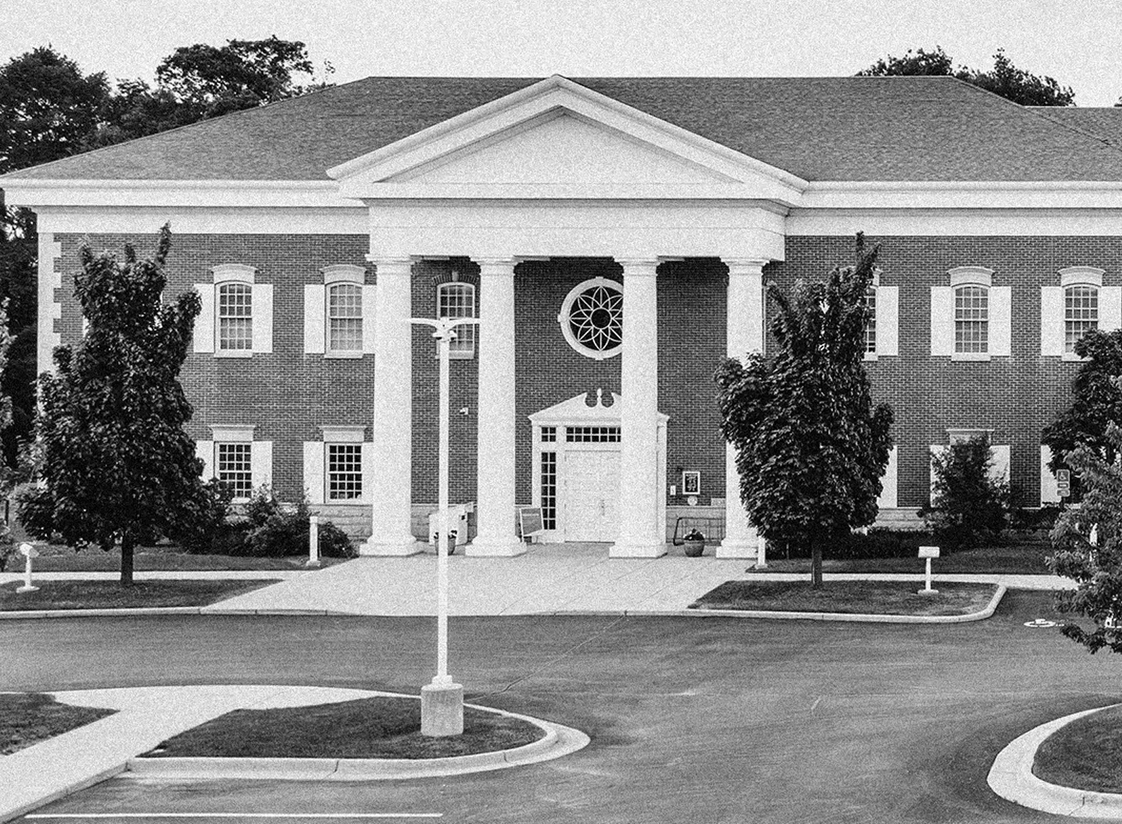Front view of a classic brick building with large white columns, arched windows, and a circular window above the entrance.