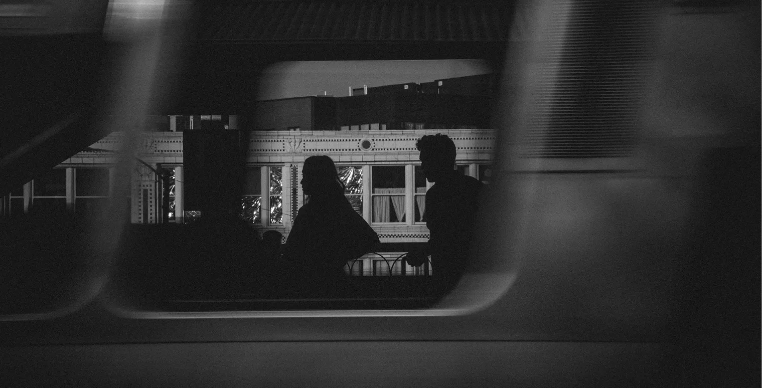 Silhouettes of two people walking past a decorative urban building in black and white.