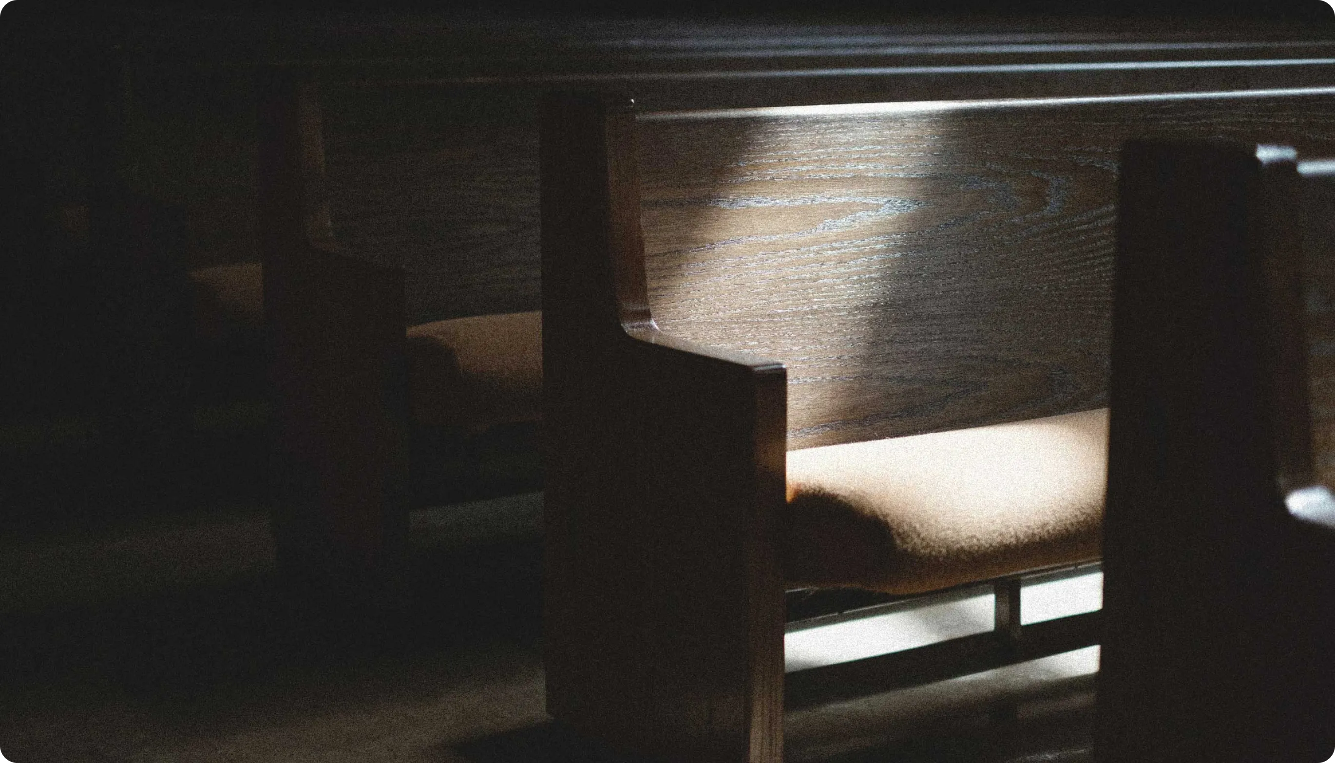 Sunlight illuminating a wooden church pew with a cushioned seat in a dimly lit space.