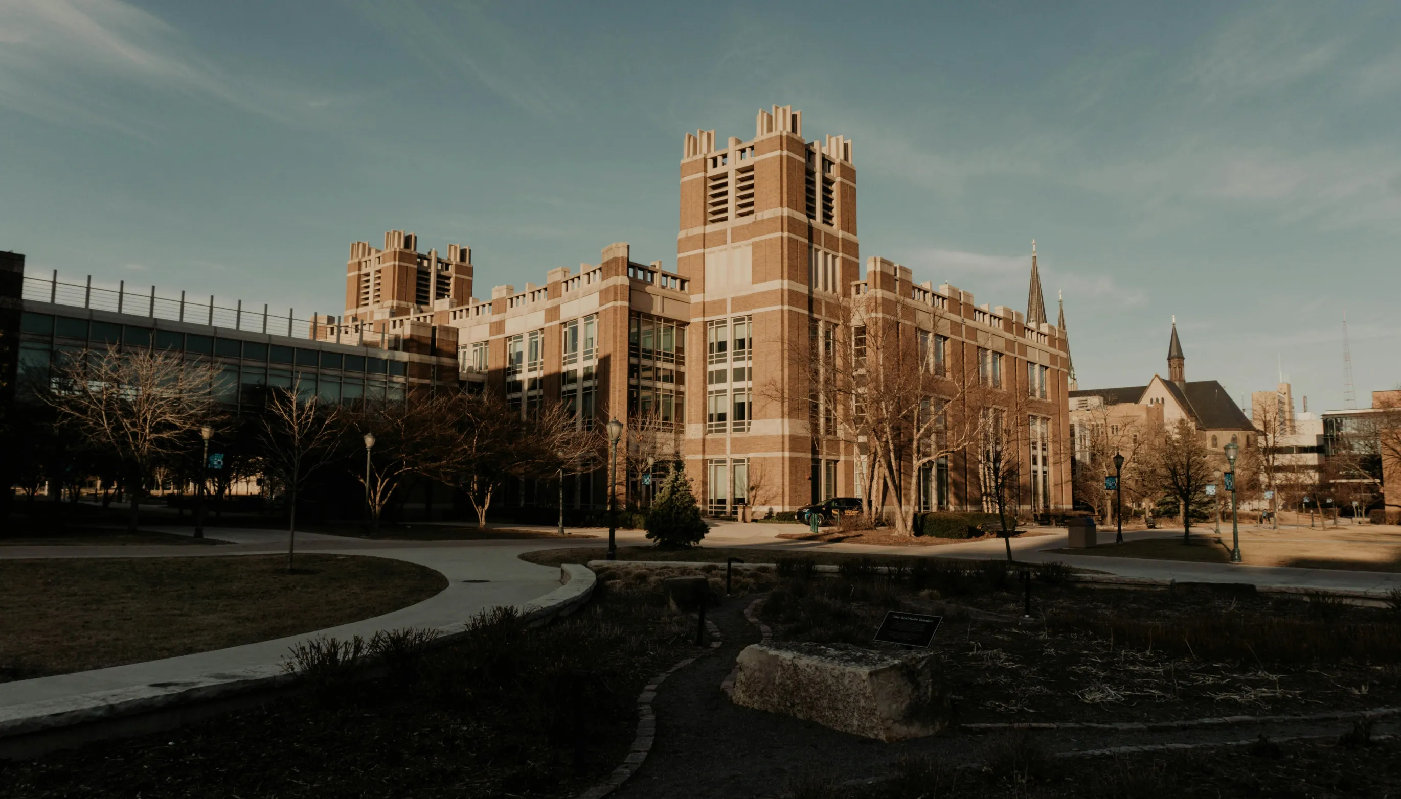 Large brick academic building with towers, surrounded by leafless trees and curved walkways at dusk.