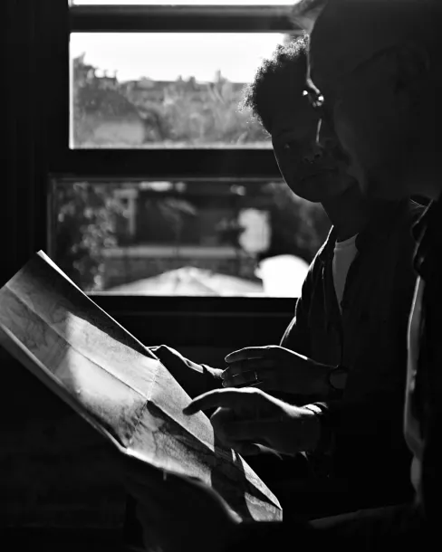 Two people sitting by a window, looking at and pointing to a large paper or map.