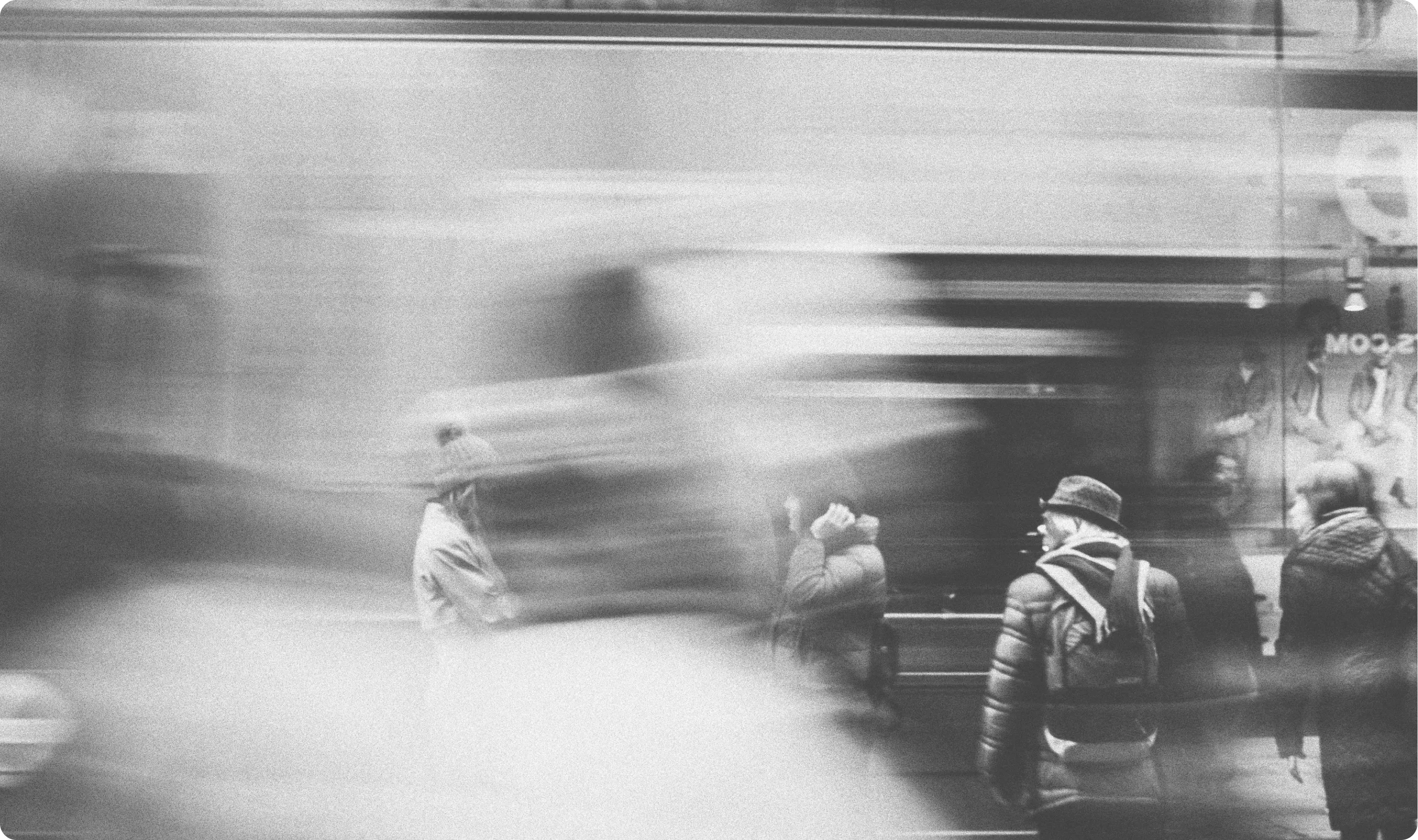 Black and white blurred street scene with people wearing winter clothes and hats.