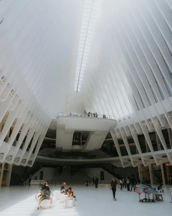 Spacious, bright white modern interior with high ceiling, people sitting and walking inside.