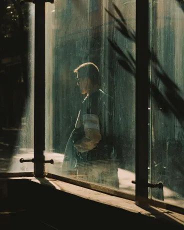 Person seen through foggy glass panels with sunlight casting shadows on the surface.
