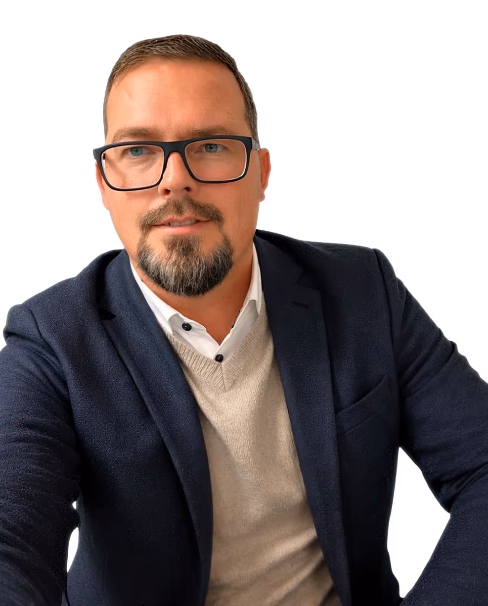 Mann mit Brille und Bart trägt weißen Kragen, beigen Pullover und dunkelblauen Blazer.