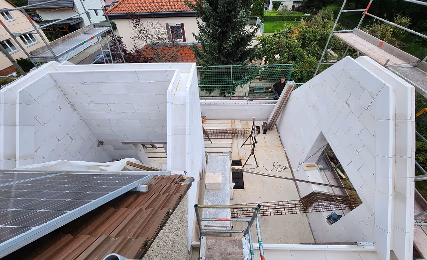 Blick auf eine Baustelle von oben mit eingerüsteten weißen Wänden und braunem Dach, auf dem Solarpaneele montiert sind.