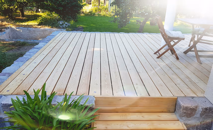 Holzterrasse mit Stufen, Gartenmöbeln und umgebendem Garten bei Sonnenlicht.