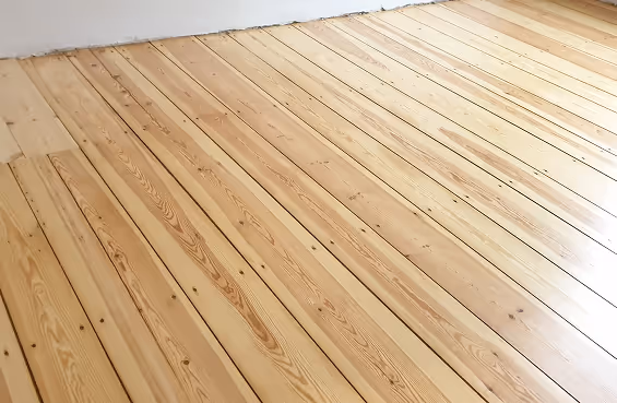 Heller, neuer Holzboden mit langen, parallelen Dielen und sichtbarer Holzmaserung nahe einer weißen Wand.