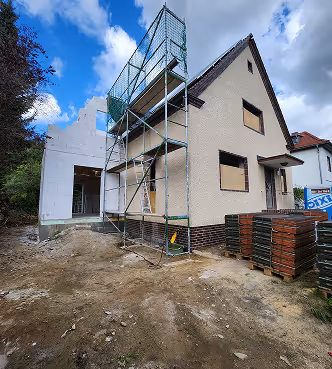 Haus unter Renovierung oder Erweiterung mit einem Gerüst neben der Eingangstür und Baustoffpaletten im Vordergrund.