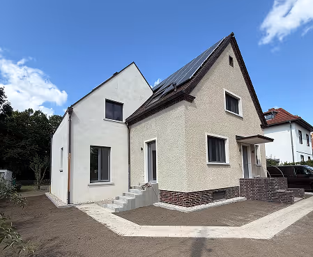 Ein modernes zweistöckiges Haus mit Solarzellen auf dem Dach und Wegplatten in einem Garten ohne Bepflanzung.