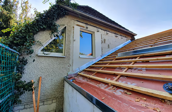 Ein Haus mit einer bewachsenen Wand und neuen Dacheindeckungen in der Bauphase unter klarem Himmel.