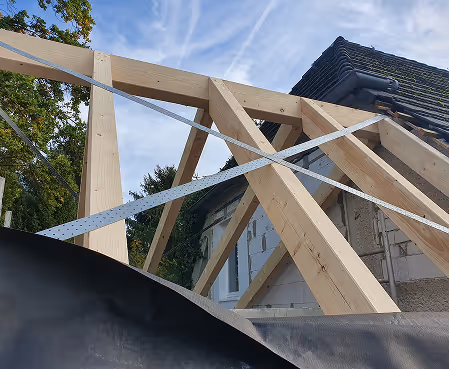 Holzrahmenkonstruktion an einem Haus unter blauem Himmel mit Bäumen im Hintergrund.