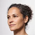 Close-up portrait of a woman with curly hair looking slightly to the left against a plain light background.
