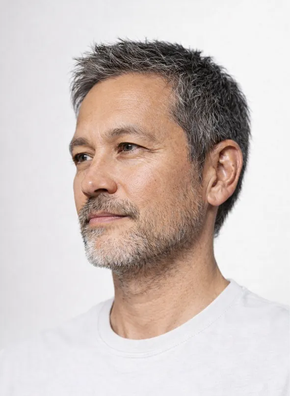 Close-up portrait of a middle-aged man with salt-and-pepper hair and beard, wearing a dark crew-neck shirt, looking slightly to the side.